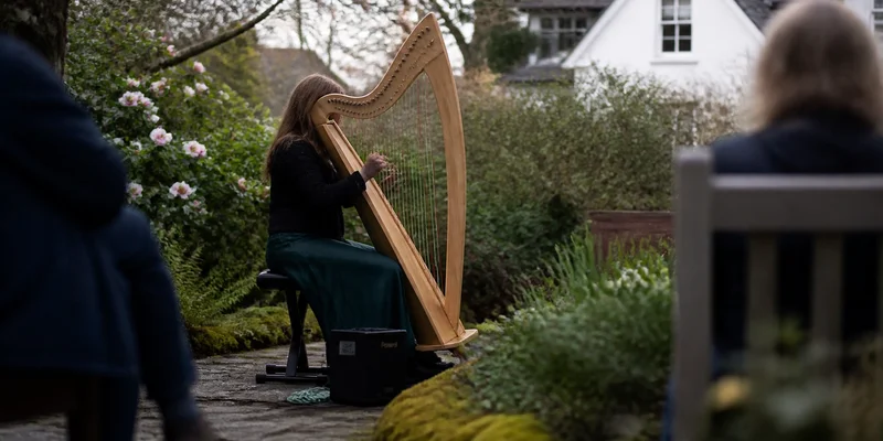 Musician playing Celtic harp in a historic manor house garden surrounded by native spring blooms Lents SE Portland Oregon